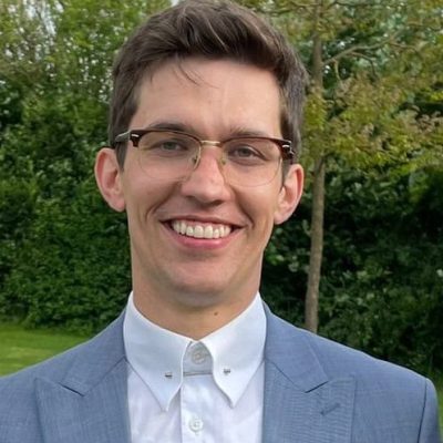 Young man in a suit smiling outdoors, public speaking confidence expert.