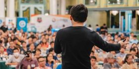 Speaker presenting confidently at No Stress Speeches event in a large hall.