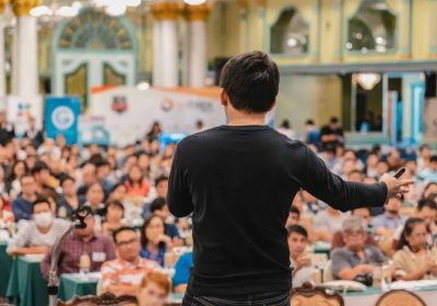 Speaker presenting confidently at No Stress Speeches event in a large hall.